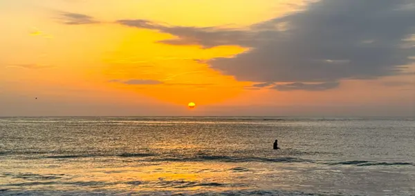 Sunset over the Atlantic Ocean in Jacksonville Beach, Florida, with a paddleboarder enjoying the calm evening waters along the coastline.