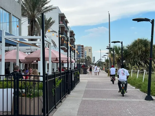 Pedestrians walking past restaurants, outdoor seating, and palm trees in the Jacksonville Beach dining district.