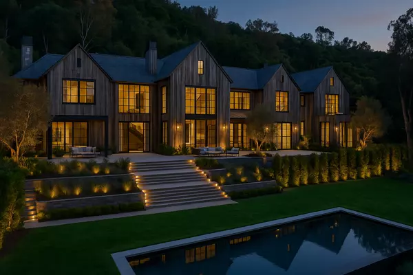 Night view of a large modern farmhouse luxury estate with landscaped steps and a reflecting pool in Los Angeles, representing home buyer services.