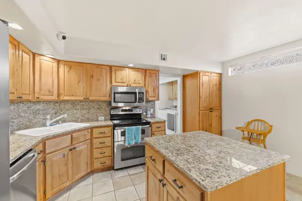 A bright kitchen view showcasing a large granite-topped island and extensive knotty pine cabinetry. The space is equipped with stainless steel appliances and leads toward a functional laundry area.