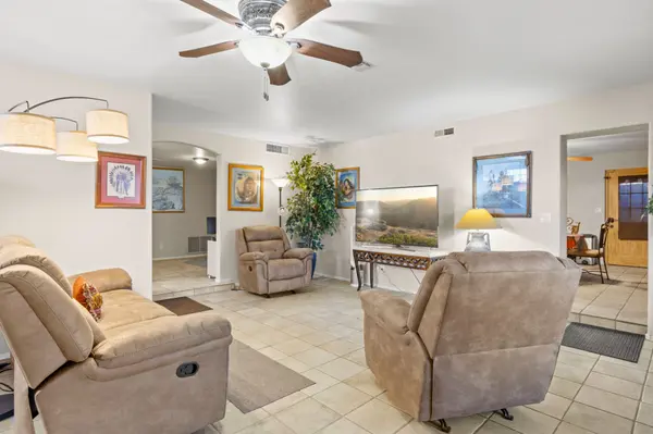 Interior view of a spacious living room in a New River, AZ home featuring neutral tile flooring, a ceiling fan, and an open-concept layout leading to other rooms. The space is decorated with Southwestern art and comfortable reclining furniture.
