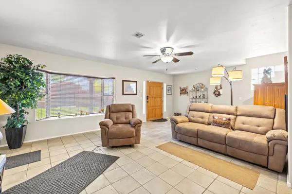 Large, bright living room with neutral tile floors, a big picture window, and a ceiling fan. The room is furnished with plush reclining sofas and decorated with Southwestern accents, creating a comfortable desert retreat.