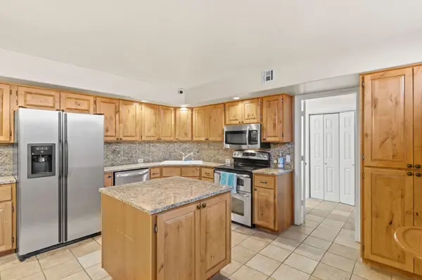 A close-up view of a functional kitchen with stainless steel appliances, a built-in microwave, and a small central island. The room is lined with extensive knotty pine cabinets and granite backsplashes.