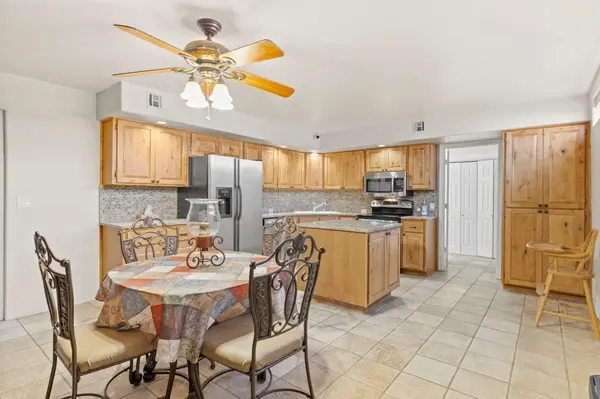 Open concept kitchen and dining area featuring warm knotty pine cabinetry, granite countertops, and neutral tile flooring. The space includes a central island and a ceiling fan, with a dining table in the foreground.