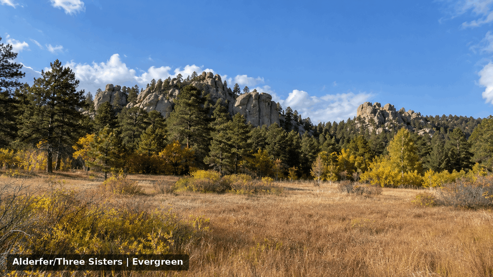 Alderfer Three Sisters Park in Evergreen, Colorado, with its distinctive granite rock formations, ponderosa pine forest, open meadow, and golden autumn foliage.