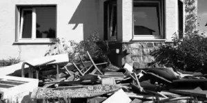 Exterior scene showing a yard cluttered with debris and damaged items in front of a house, conveying abandonment or foreclosure conditions.