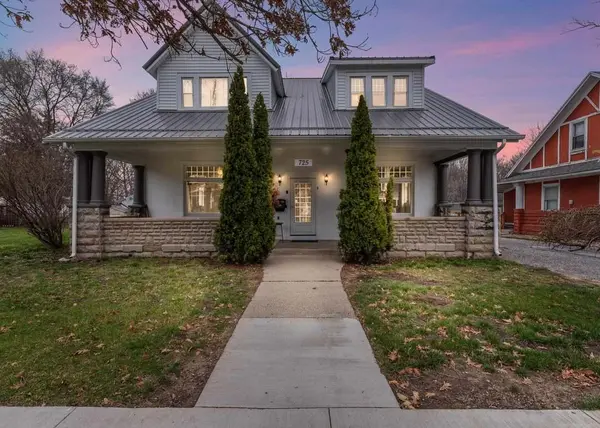 Charming historic Indiana home with a spacious covered front porch, stone columns, and warm exterior lighting at dusk.