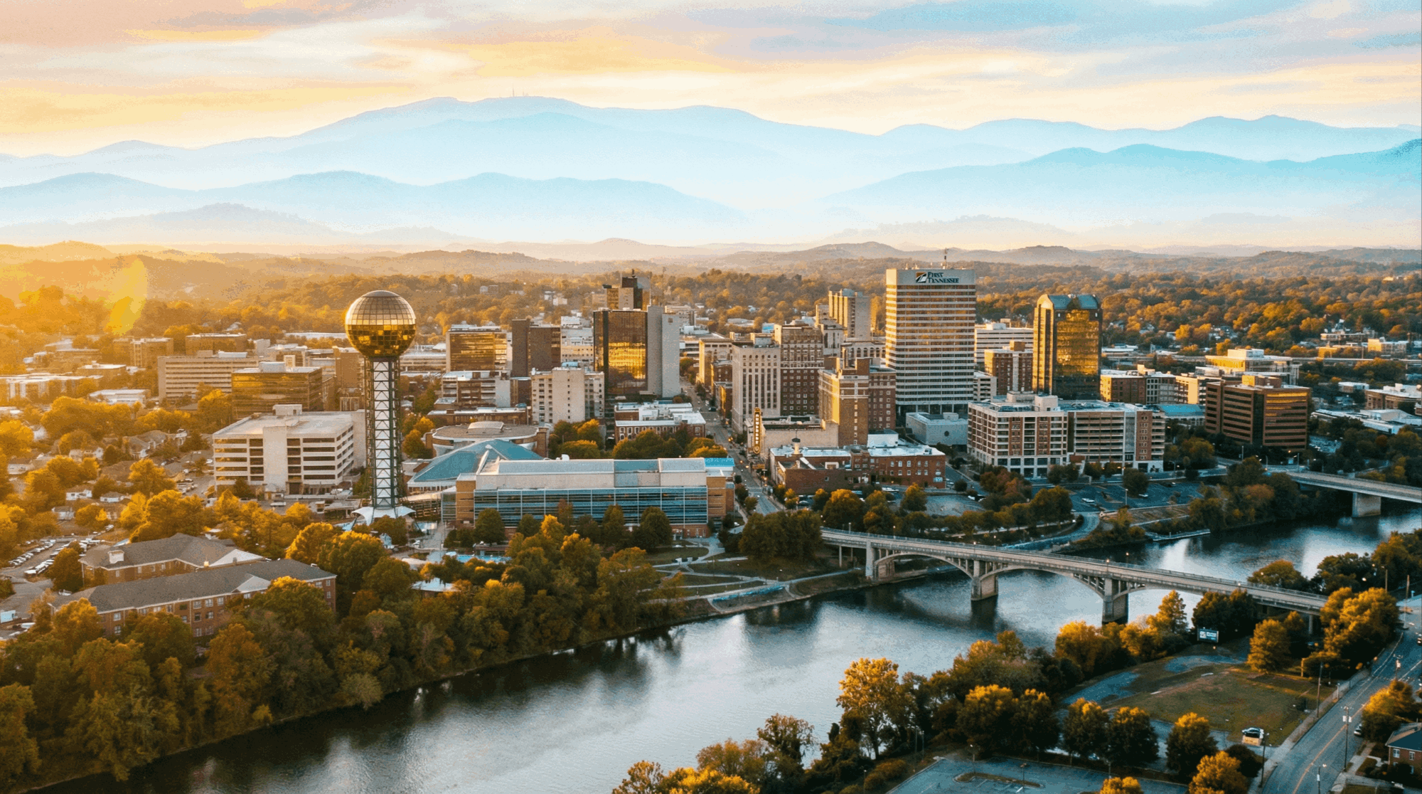 An aerial view of the Knoxville, Tennessee skyline with the majestic Smoky Mountains in the background, bathed in the warm glow of golden hour lighting.