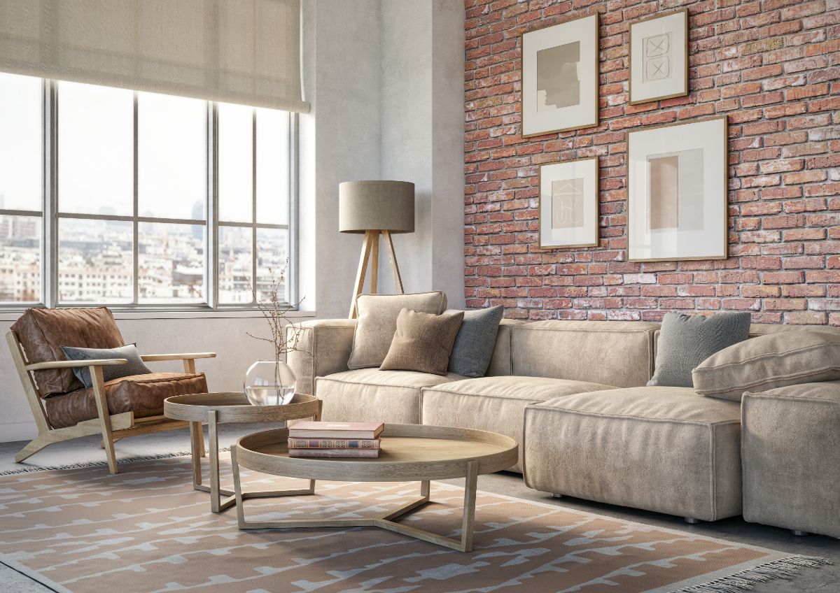 Bright loft-style living room with large industrial window, exposed brick accent wall, comfortable sectional sofa and natural light filling the room.