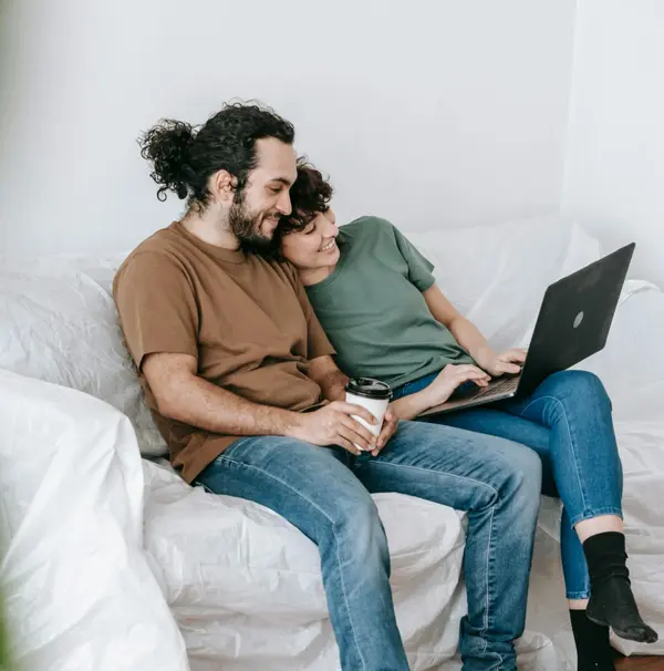 Couple sitting together on a couch, browsing homes online on a laptop