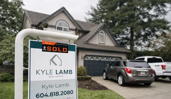 Kyle Lamb Real Estate “Sold” sign on a front lawn in front of a suburban two-story home, with cars in the driveway and trees in the background on an overcast day.