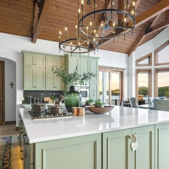 Circular cropped interior kitchen photo: bright kitchen with central island, light green cabinets, wooden ceiling beams, and pendant lights