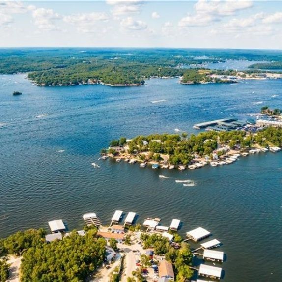 Circular aerial lake view photo: blue water, shoreline with docks and small islands, sunny sky