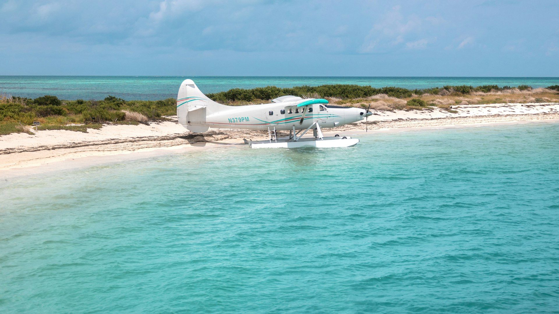 Seaplane parked on a white-sand beach beside turquoise Gulf water in Florida