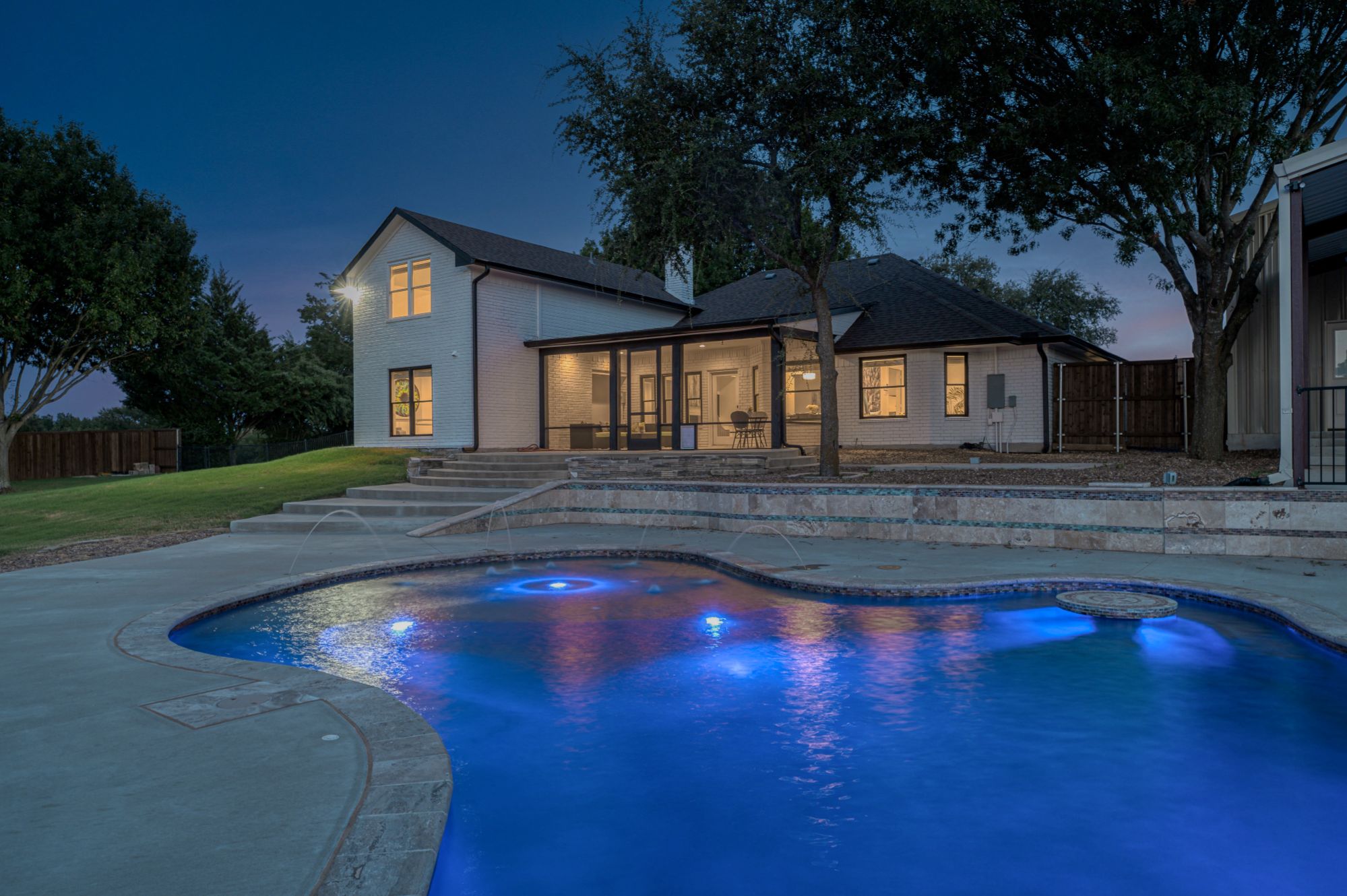 A lit up swimming pool at night with a Texas style brick home in the background.