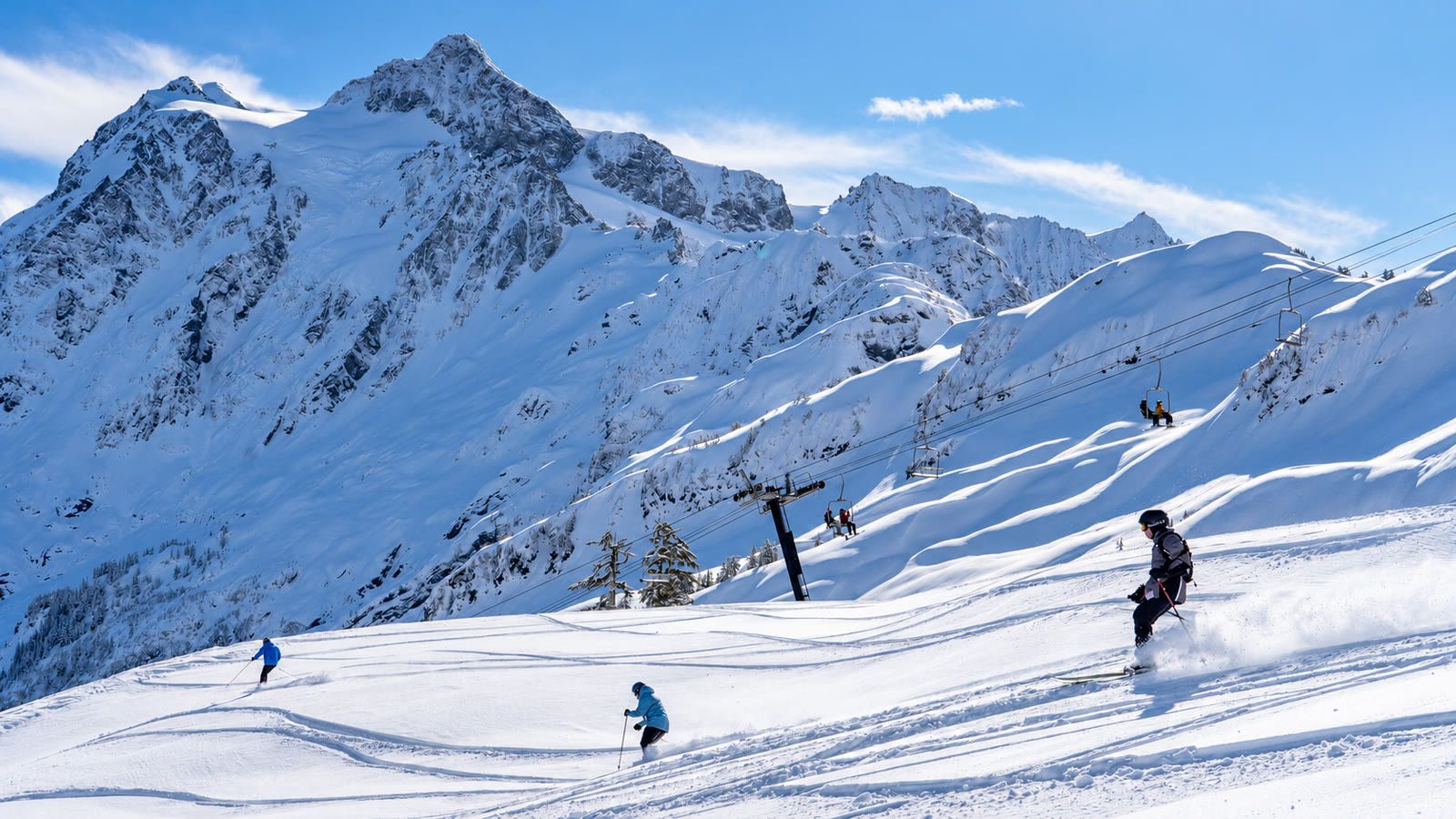 Skiers on sunny groomed runs at Mt. Baker Ski Area below Mt. Shuksan.