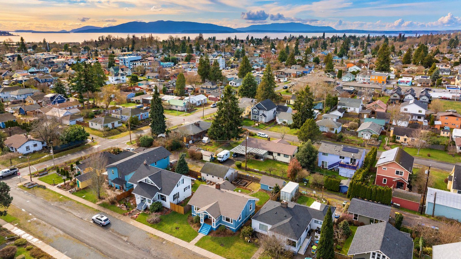 Late-day aerial view over a Bellingham neighborhood of colorful bungalows and cottages, with Bellingham Bay and Lummi Island beyond.