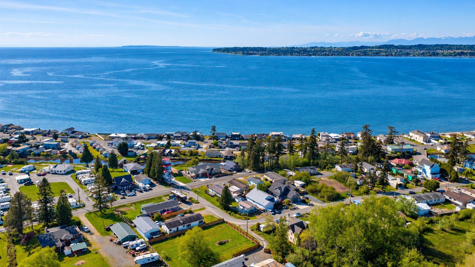 High aerial view over neighborhoods in the Birch Bay and Blaine area of Whatcom County, with the bay and the far shoreline on the horizon.