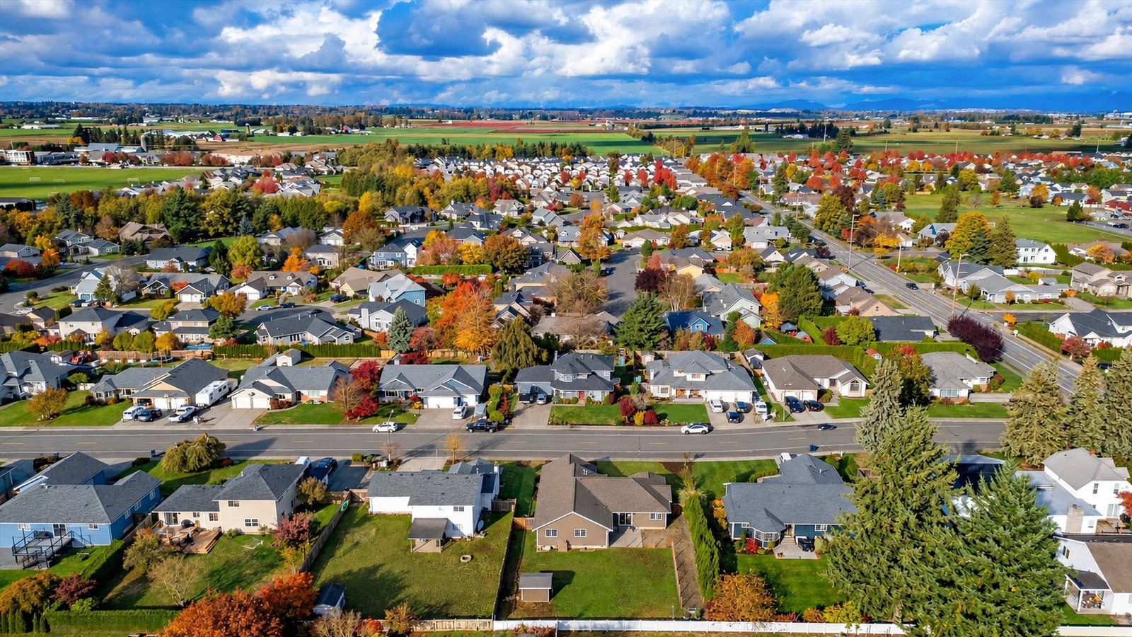 Fall aerial view over Lynden, Washington neighborhoods and tree-lined streets stretching to farmland and the mountains.