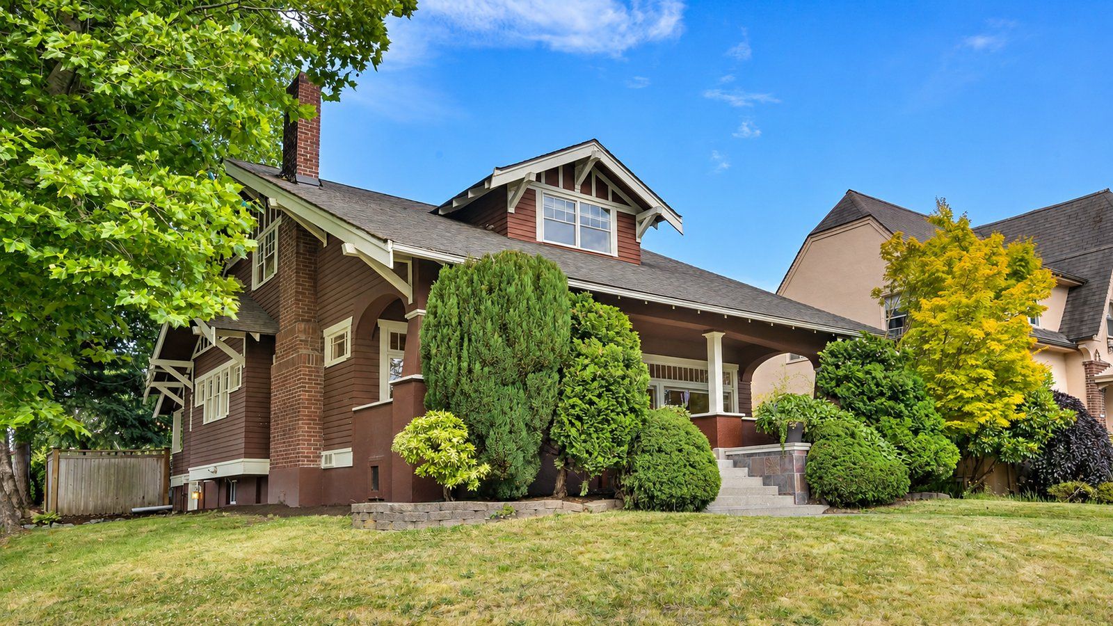A classic brick-and-wood craftsman home in Bellingham with trimmed shrubs and a freshly mowed front lawn under a blue sky.