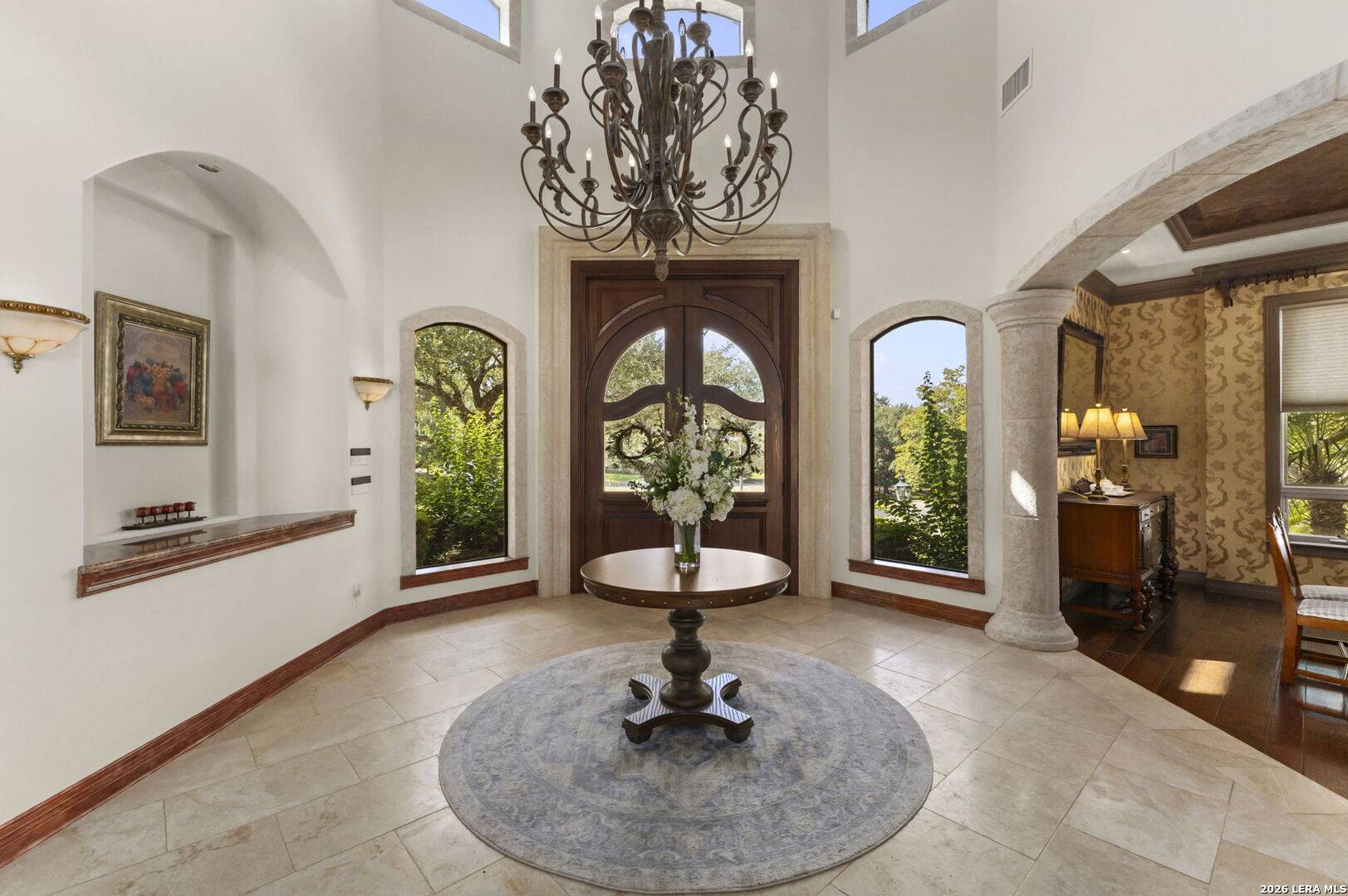 Travertine foyer of 2 Belcourt Place with mahogany double entry doors, iron chandelier and arched windows