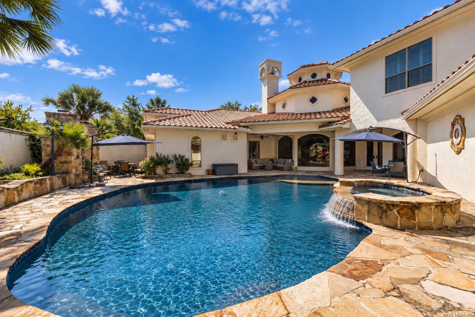 Heated pool and spa with stone waterfall at 2 Belcourt Place, framed by the Mediterranean rear elevation