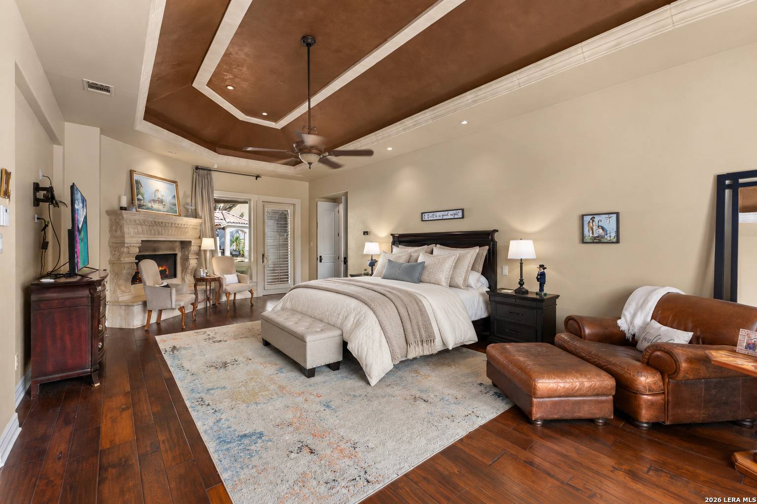 Main-level primary suite of 2 Belcourt Place with tray ceiling, wood floors and imported-marble fireplace
