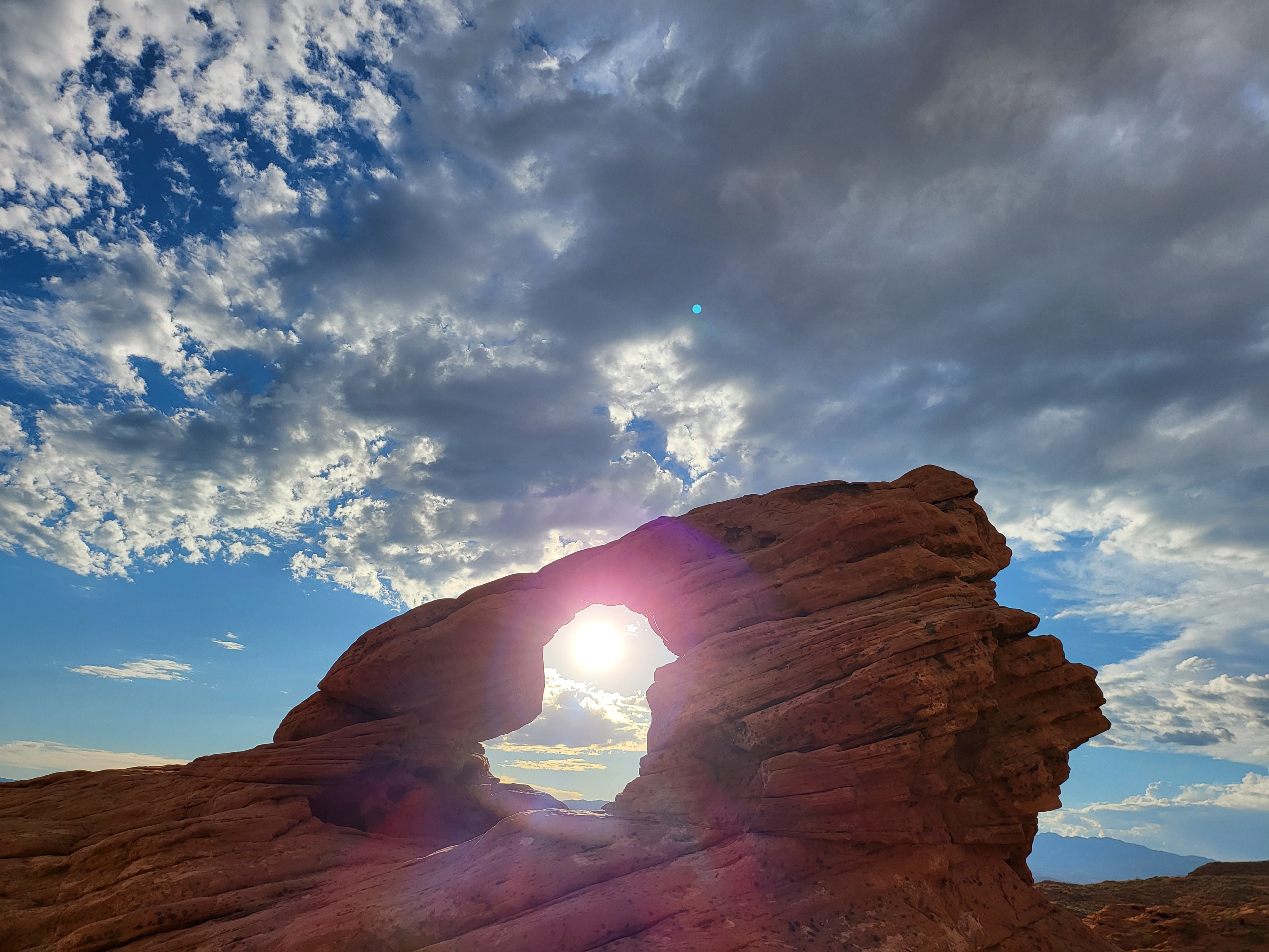 Sunlight streaming through a red rock arch formation in St. George Utah against dramatic desert sky