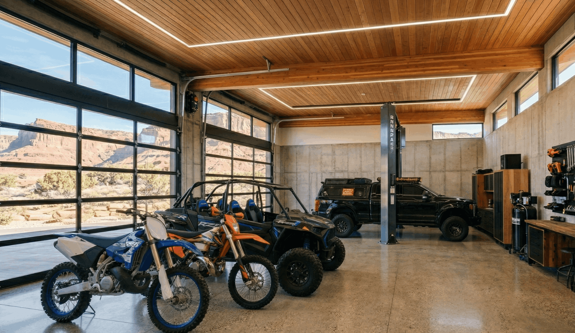 Luxury desert modern home with oversized garage, black Jeep Wrangler and RZR side-by-side parked on paver driveway, red rock canyon backdrop, St. George Utah
