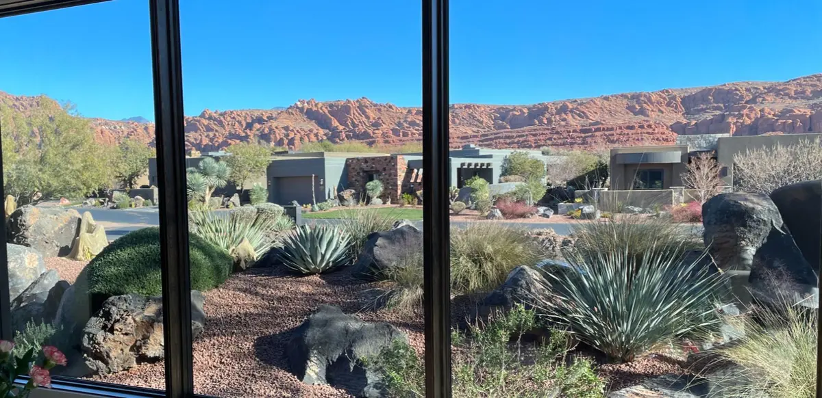 Interior view from a modern dining room with large black-framed windows showcasing a crisp, daytime desert landscape of red rock formations and desertscaped luxury yards.