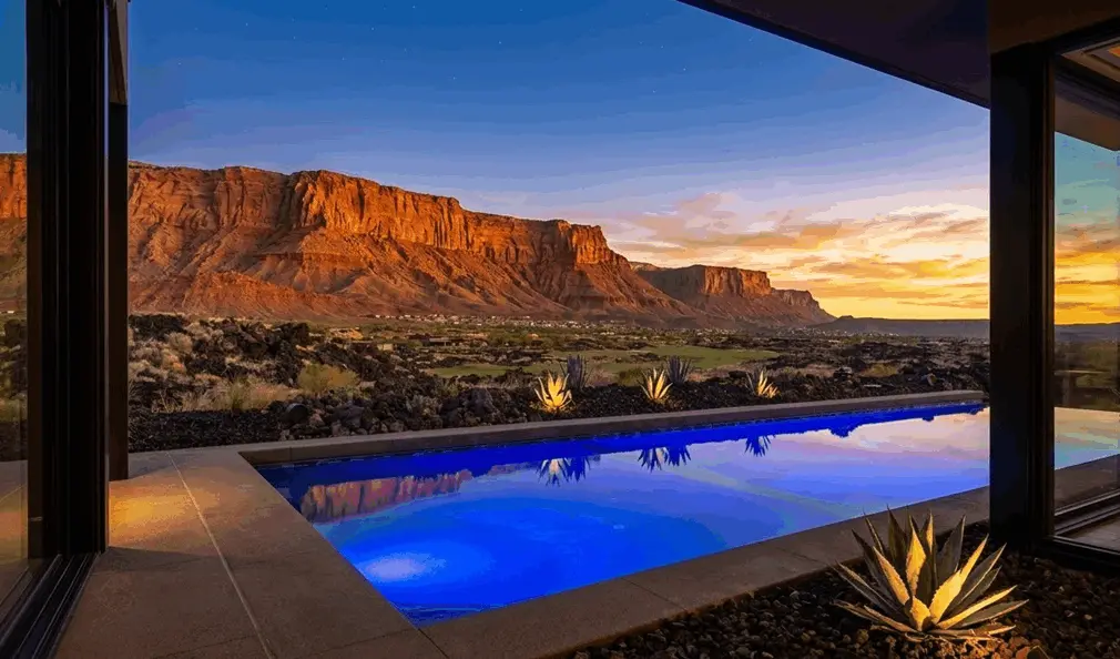 Luxurious desert residence at sunset featuring an illuminated lap pool and panoramic vistas of towering red cliffs under a dramatic golden sky.