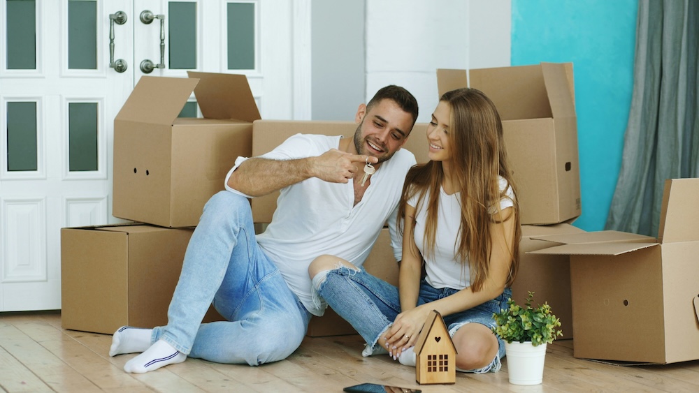 Young couple holding new house keys among moving boxes after buying their first Nevada County home