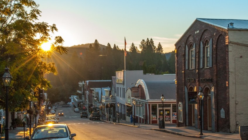 Historic downtown Nevada City street at sunset lined with brick storefronts and pine forest hills