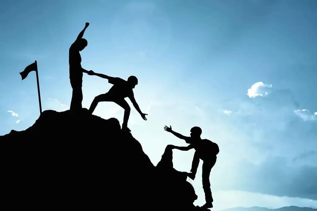 Silhouette of three boys climbing a hill, helping each other.