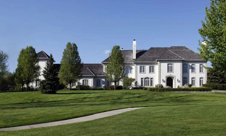 A mansion with white walls, a gray roof, and a huge lawn.