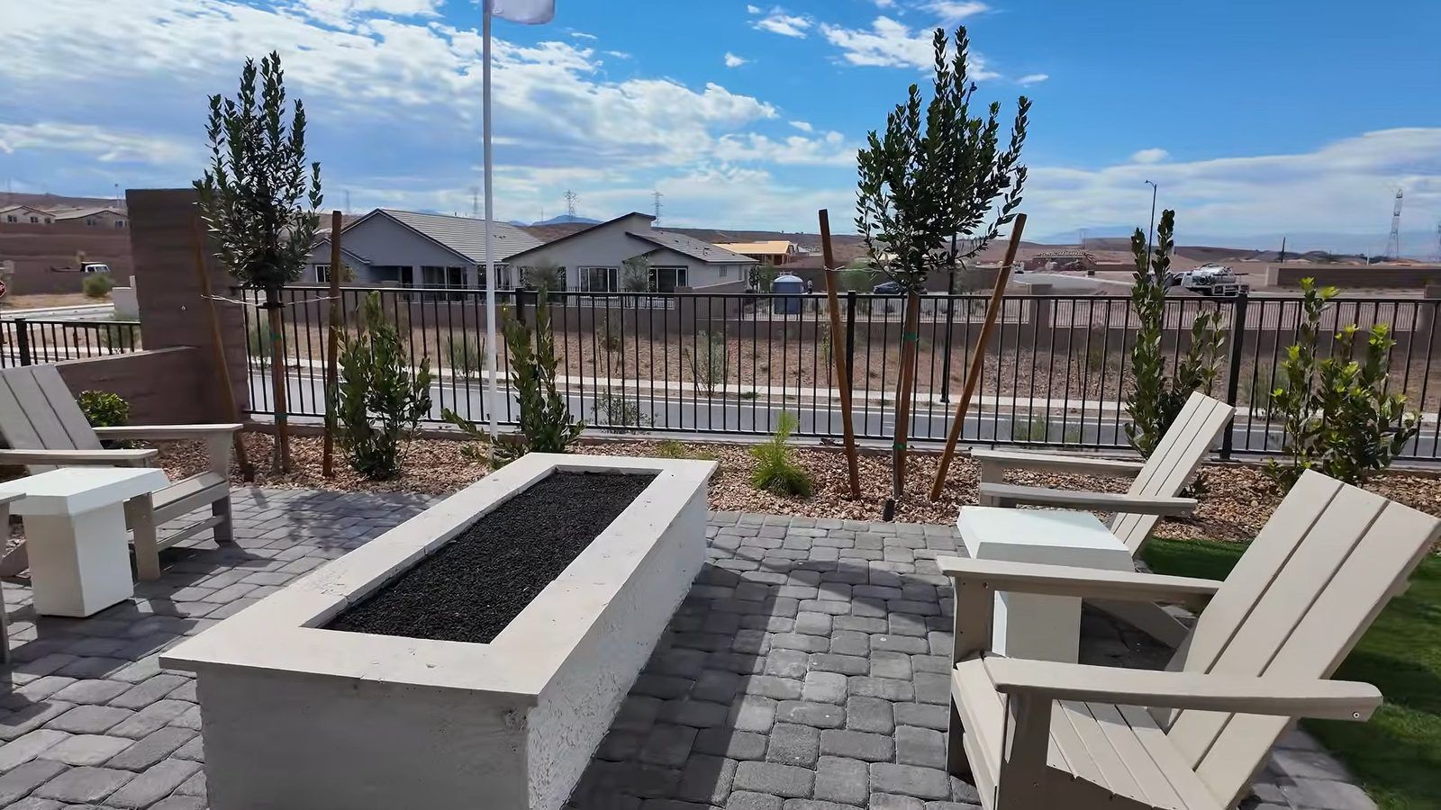 Model backyard at the Parklane with pavers, a fire table, and outdoor seating, with new homes in the distance