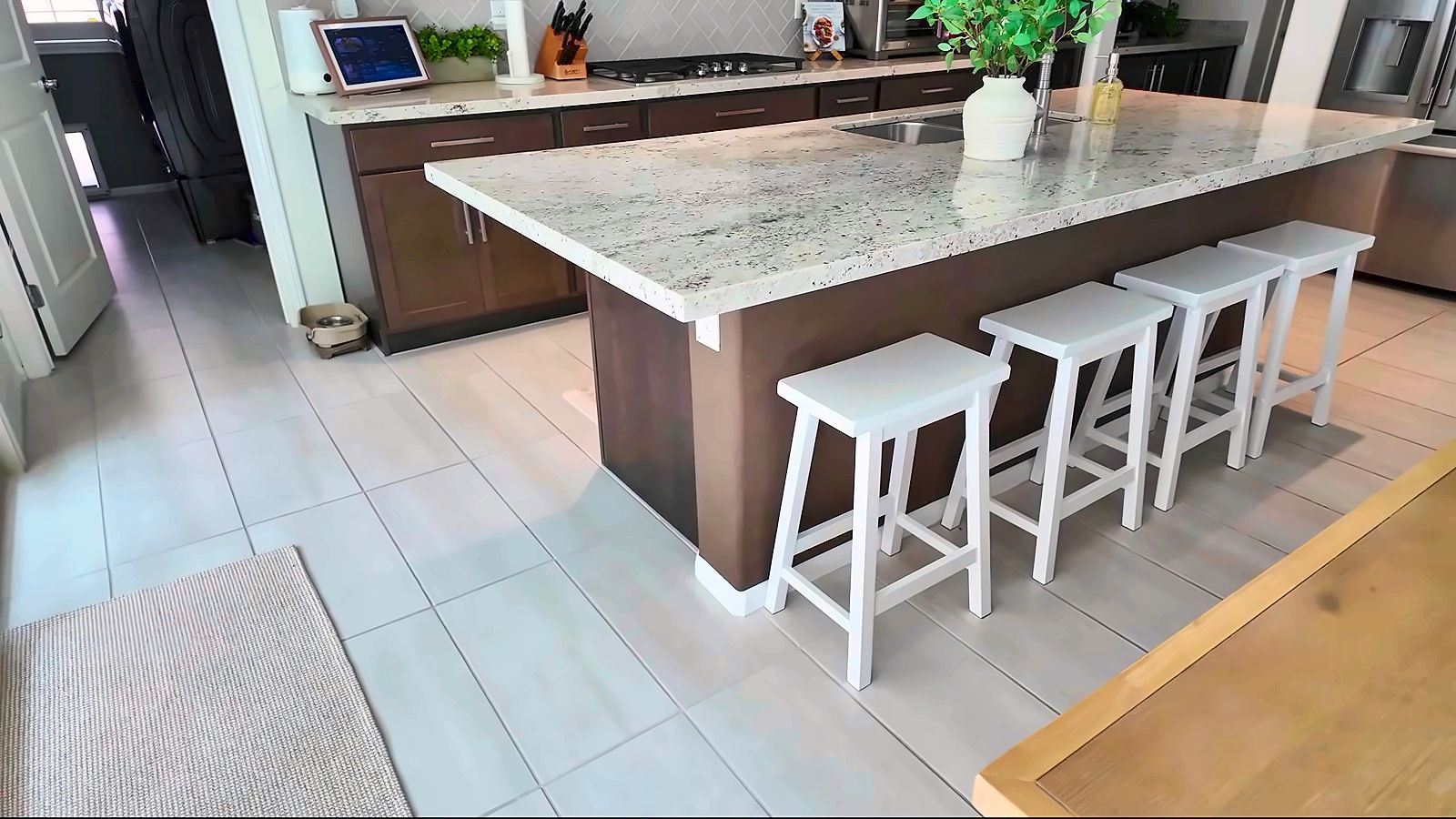 Kitchen island with a light granite top, four white bar stools and a single plant