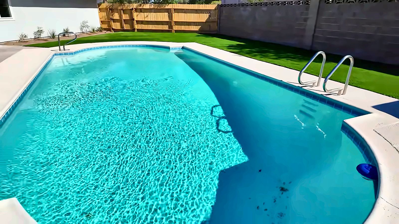 Sparkling backyard pool with a white deck, green lawn and wood fence behind a Henderson home