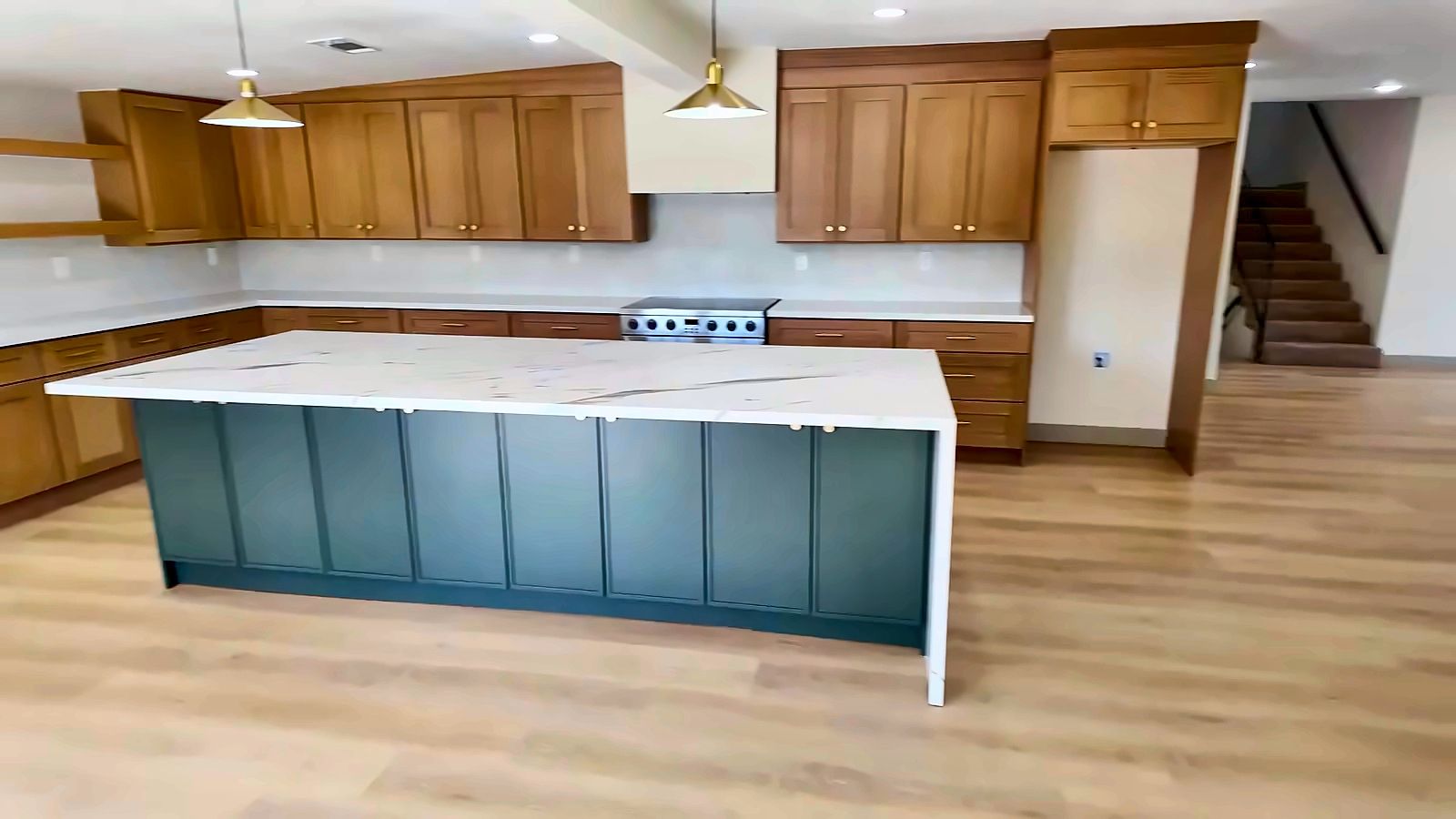 Remodeled kitchen with a large white-topped island on a dark green base, wood cabinets and brass pendant lights in a Henderson home