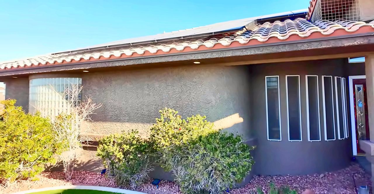 Tile roof with solar panels on a single-story Henderson home with desert shrubs in front