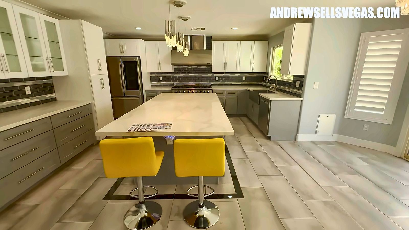 Remodeled kitchen with a long quartz island, yellow bar stools and white upper cabinets in a Rhodes Ranch home