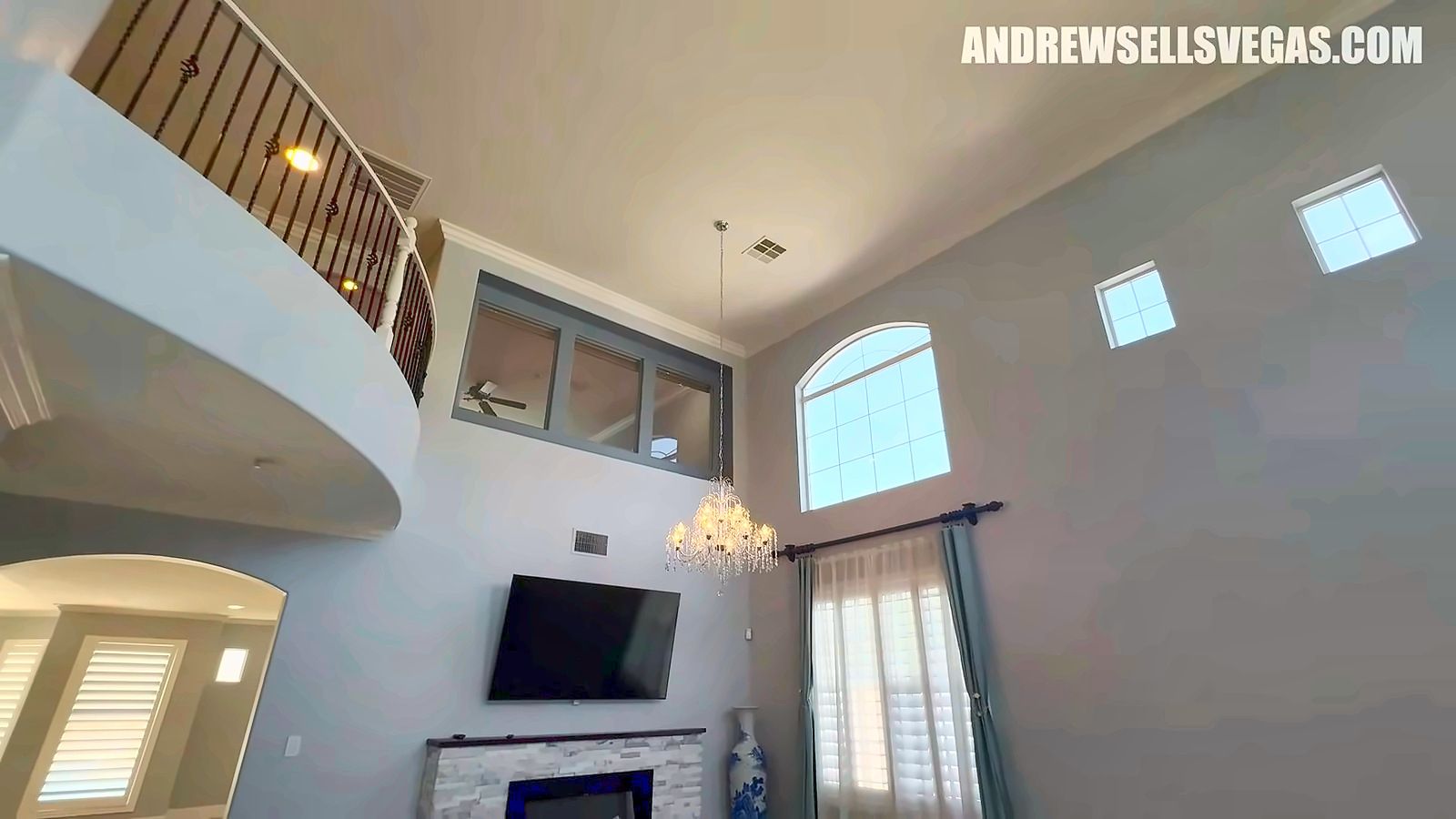 Two-story living room with tall windows, a loft railing above and a fireplace wall in a Rhodes Ranch home