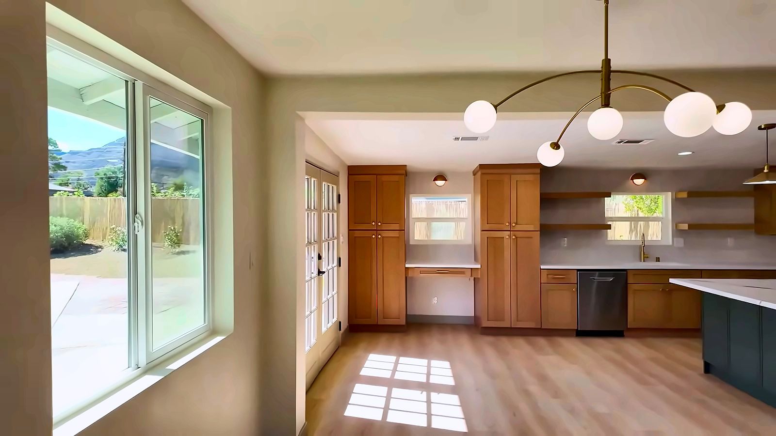 Dining area with a modern globe chandelier, a sliding door and an open kitchen with wood cabinets in a Henderson home