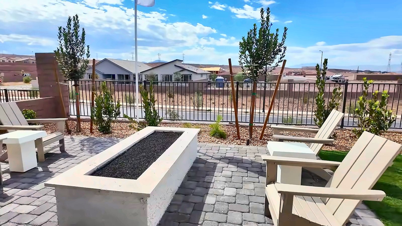 Model backyard at the Parklane with pavers, a fire table, and outdoor seating, with new homes in the distance