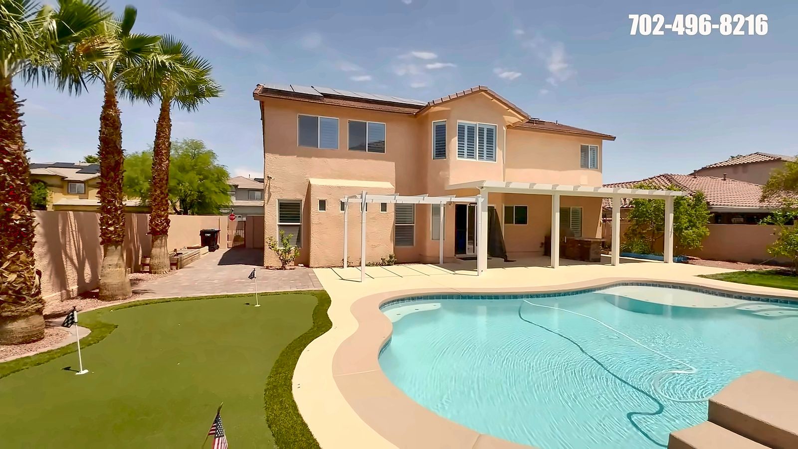 Backyard with a pool, putting green and palm trees behind a two-story Rhodes Ranch home