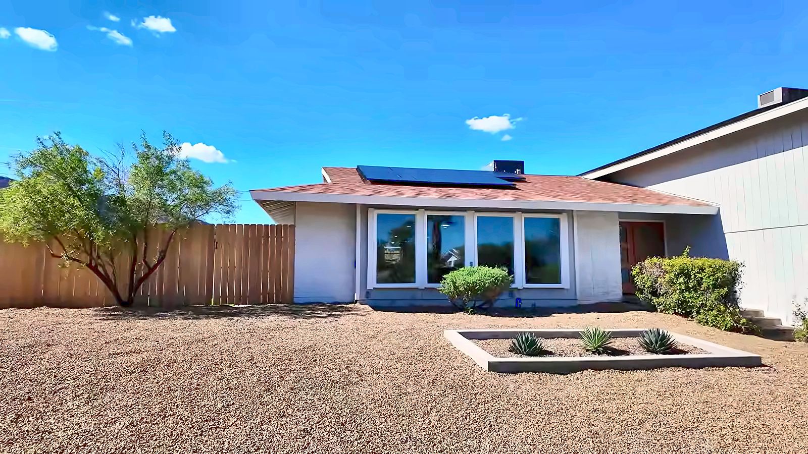 Front of a Henderson home with solar panels, a gravel front yard, a planter of agaves, trimmed shrubs and a desert tree