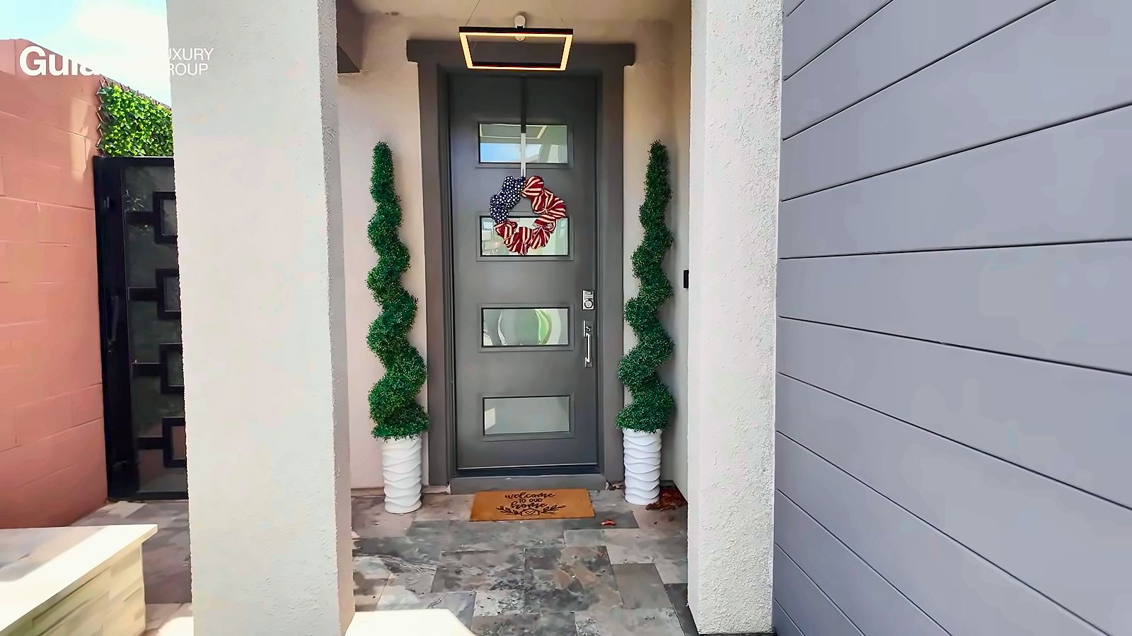 Front entry with a dark modern door, spiral topiaries in white planters and a stone-tile walkway