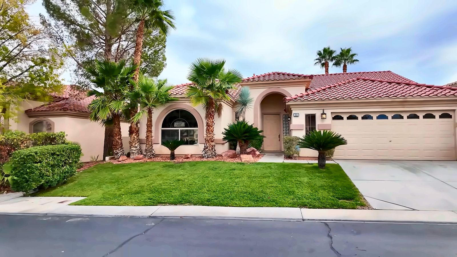 Single-story homes with tile roofs, palm trees and green lawns on a street in Rhodes Ranch, Las Vegas