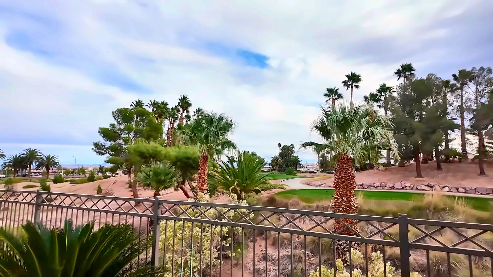 View of the Rhodes Ranch golf course and palm trees over a wrought-iron fence from a home's backyard