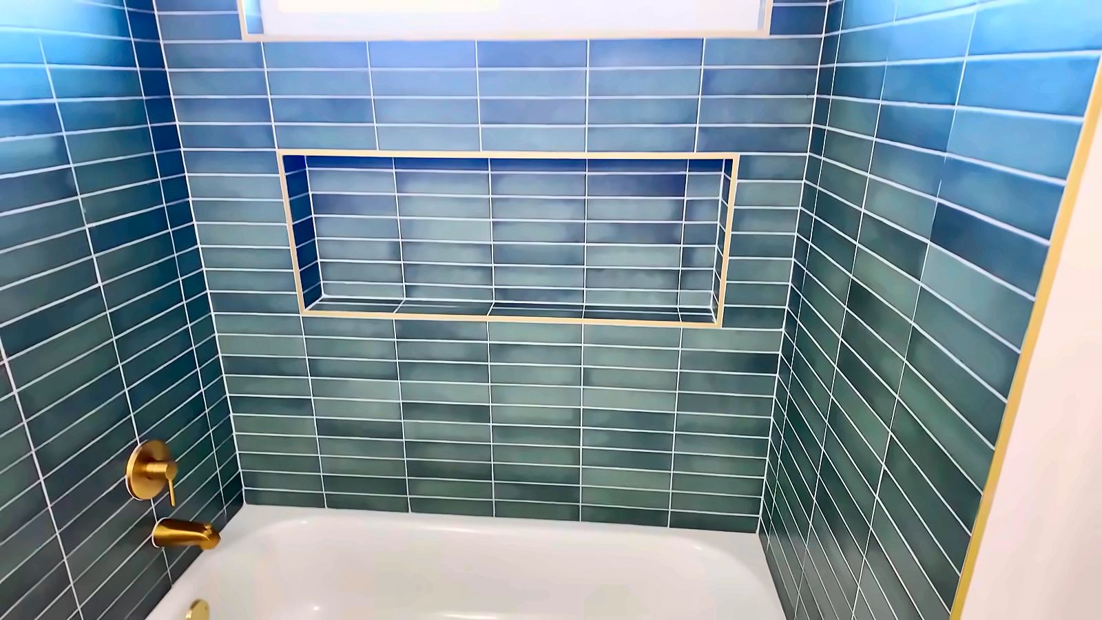 Tub and shower with blue-green vertical tile, a built-in niche and brass fixtures in a Henderson home